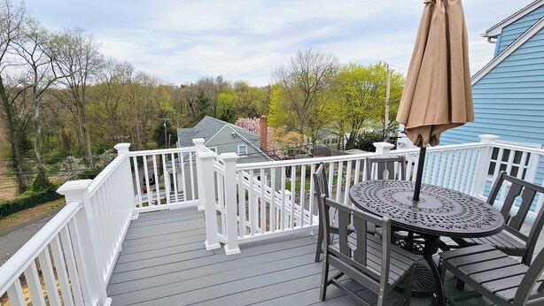 A wooden deck with a table and chairs, a white railing, and a blue house in the background.