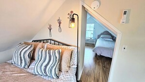 A bedroom with a sloped ceiling, a bed with patterned bedding, a bedside lamp, and a wall-mounted light fixture.