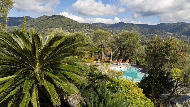 A pool area with lounge chairs, surrounded by lush greenery and mountains in the background. - Villa San Massimo with pool by Wonderful Italy (Rapallo)