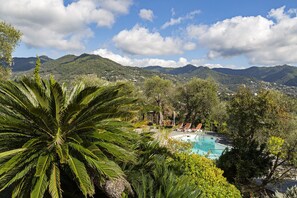 A pool area with lounge chairs, surrounded by lush greenery and mountains in the background.