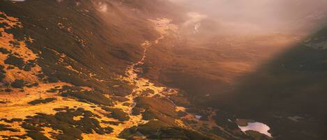 A mountainous landscape with a valley, a small lake, and a trail.