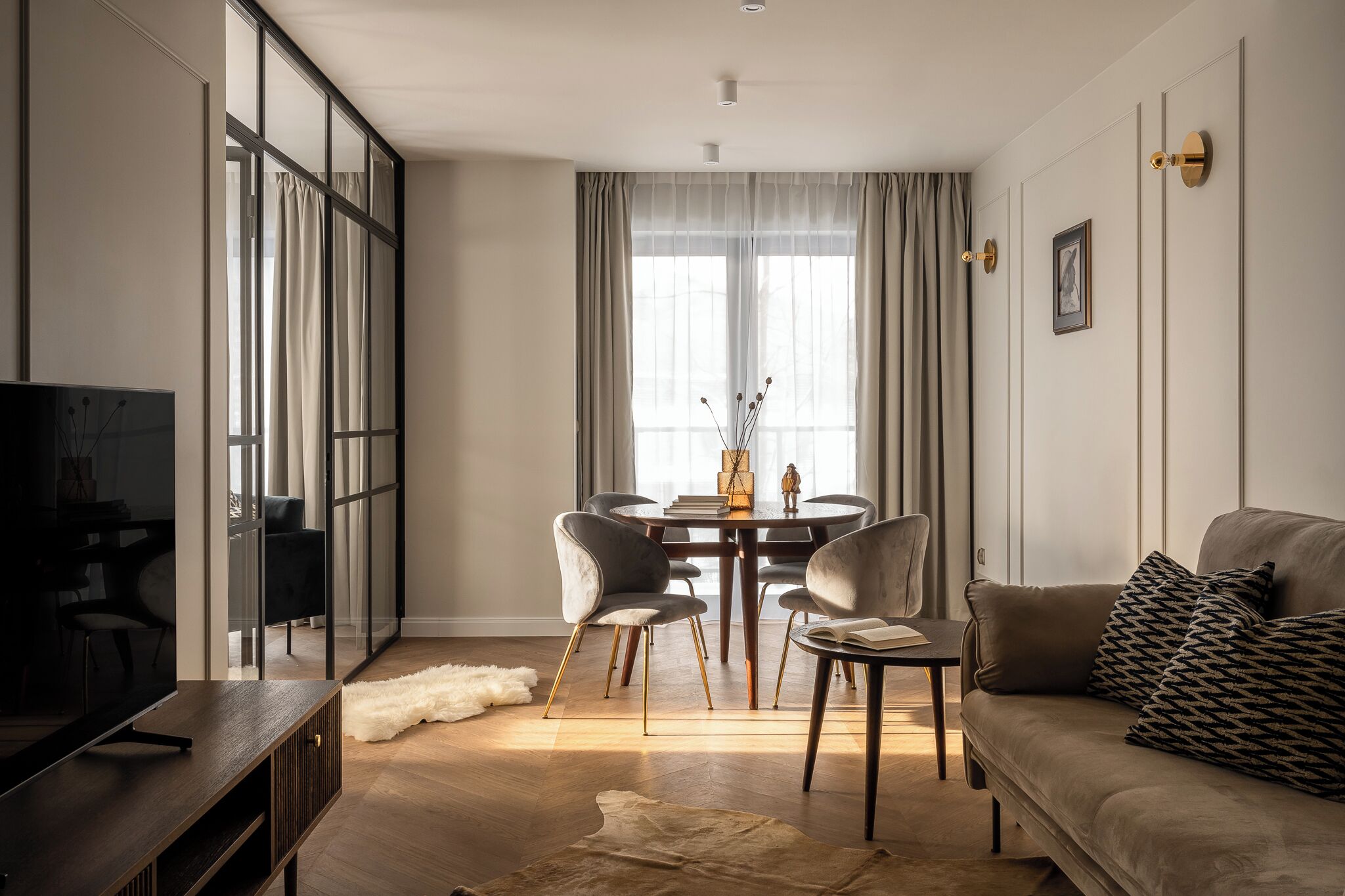 A modern living room with a sofa, a coffee table, a TV, and a dining area with chairs and a table.