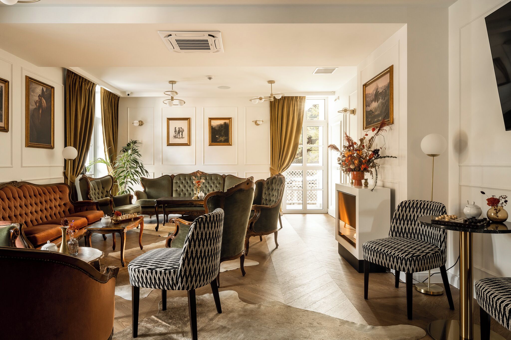 A spacious living room with a brown leather sofa, green armchairs, and a patterned table.