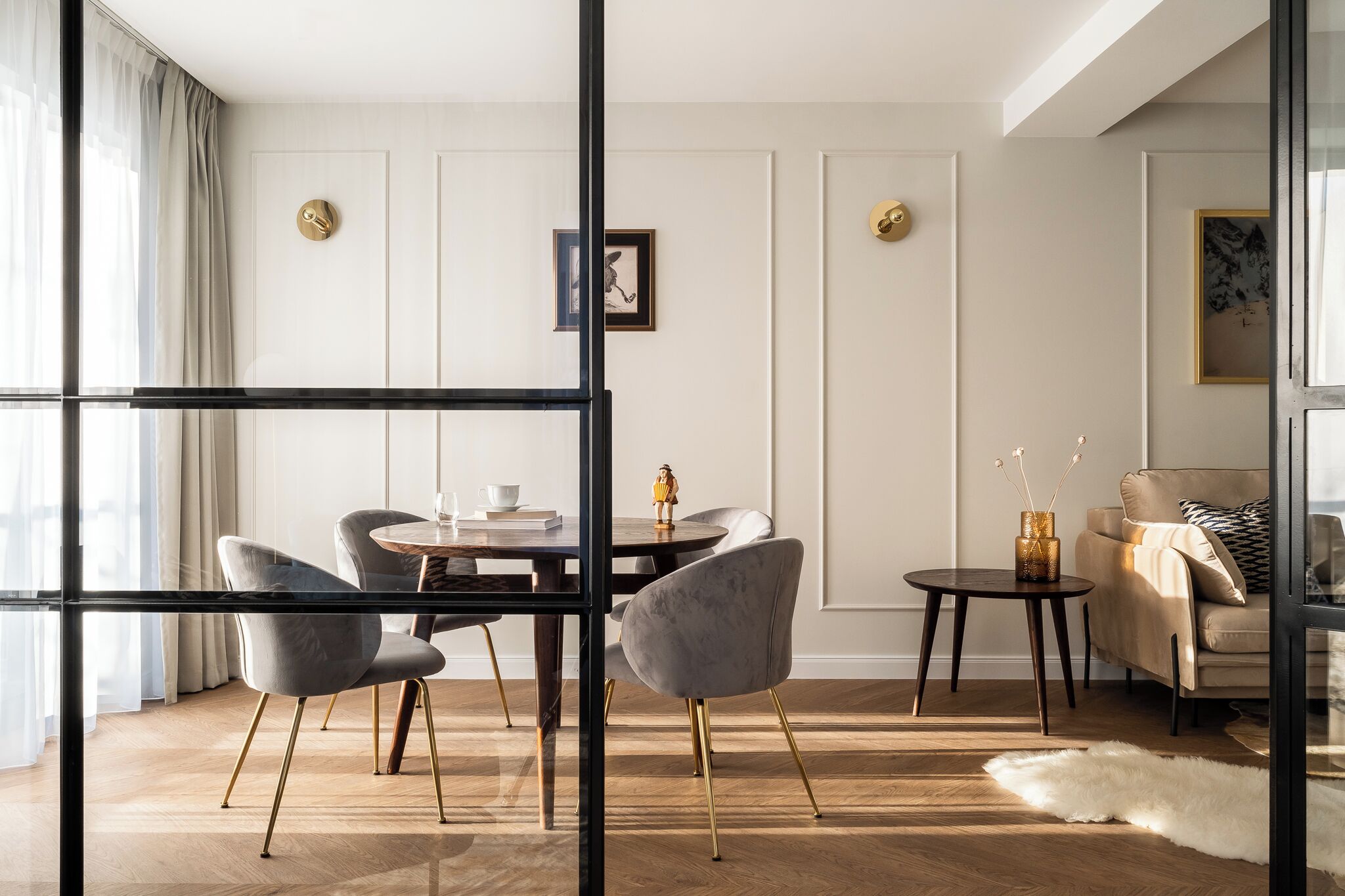 Una sala moderna con una mesa redonda de comedor, sillas tapizadas en gris, un sofá color beige y una mesa de centro de vidrio.