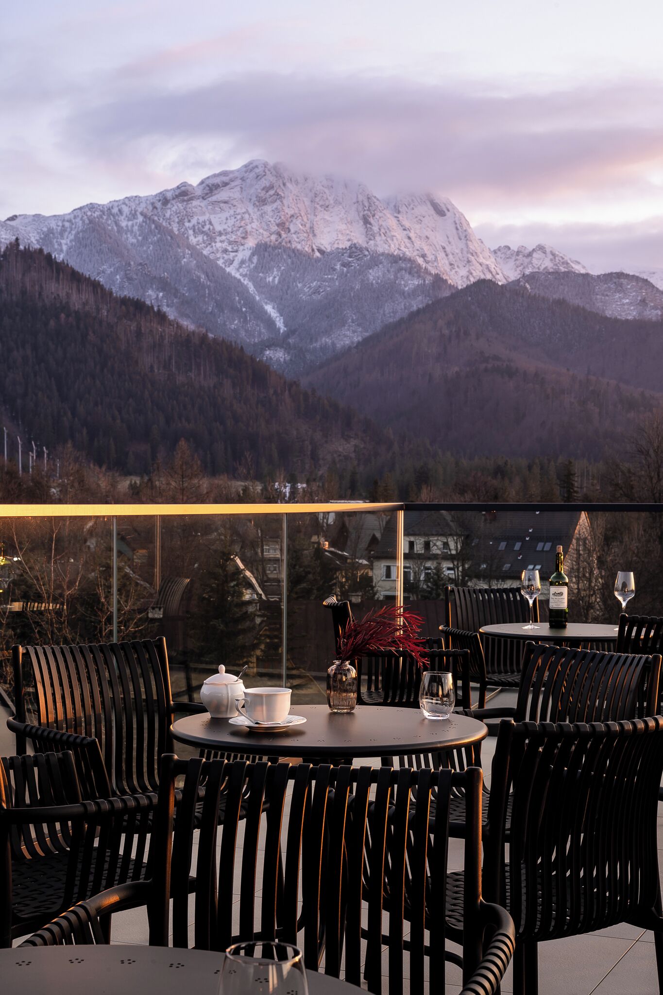 A terrace with round tables and chairs, a bottle of wine, and a teapot.