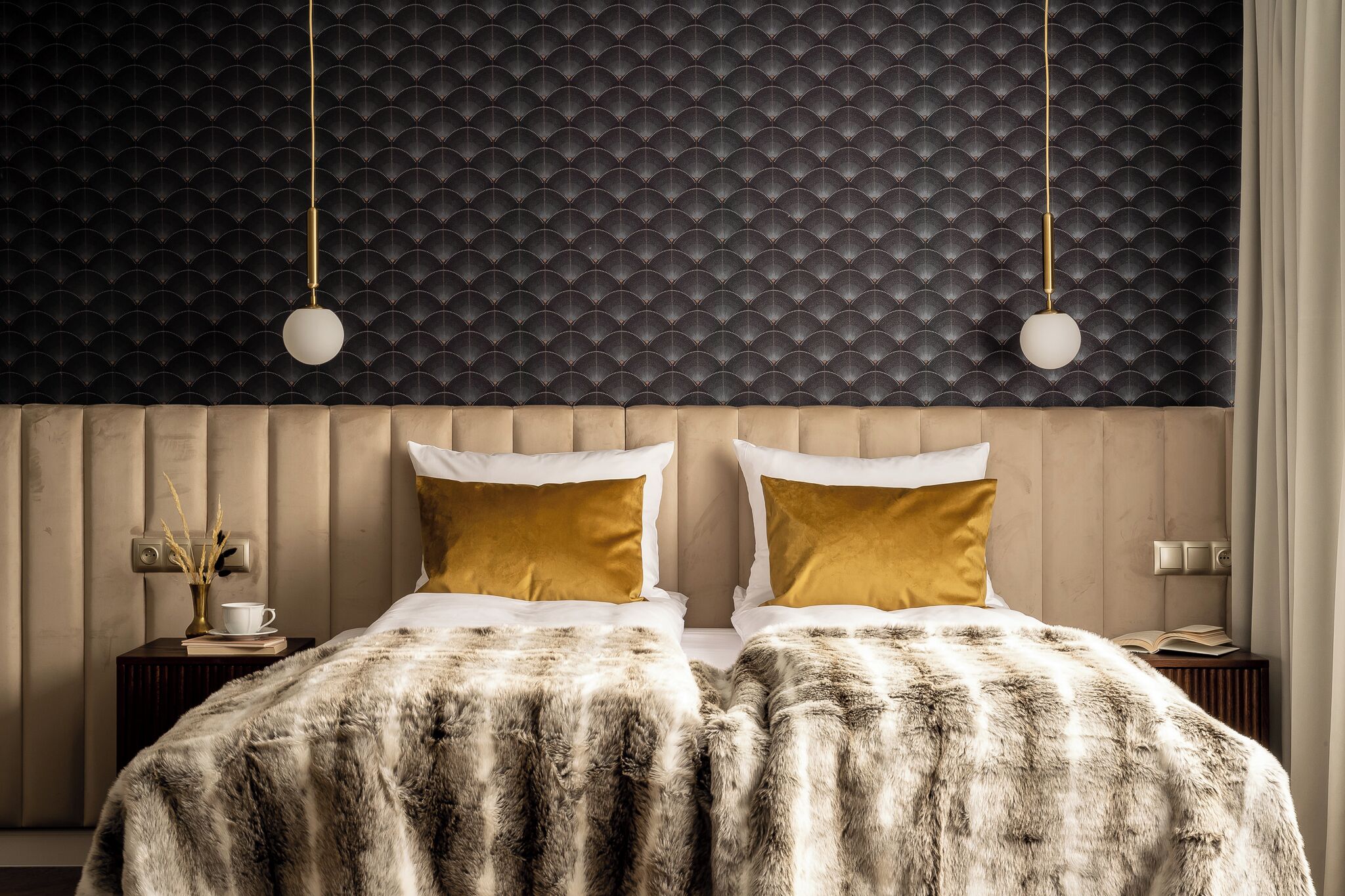 A bedroom with a tufted headboard, two gold pillows, a fur throw, and a pendant light.