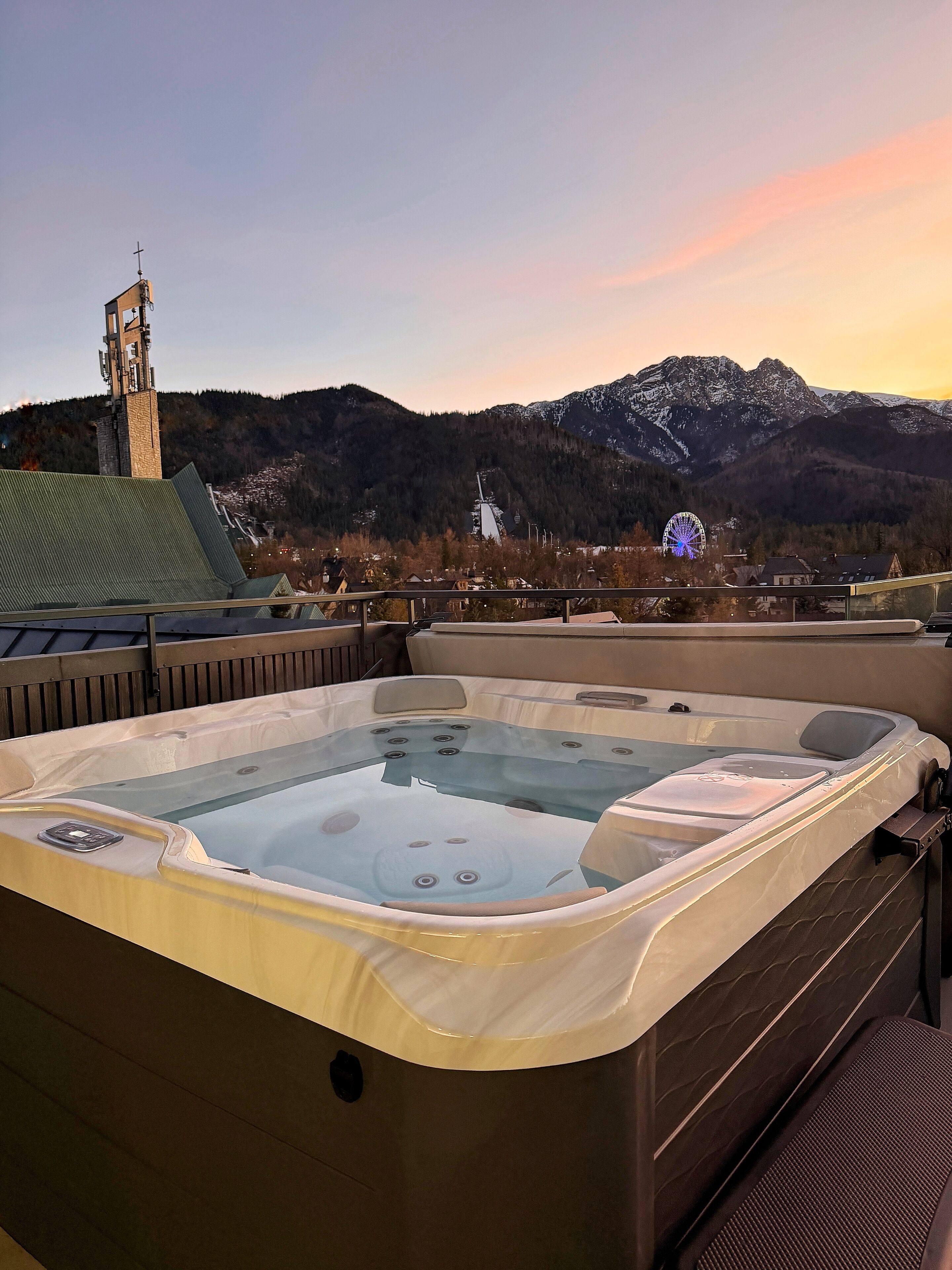 A hot tub with a view of a mountain range and a Ferris wheel in the background.