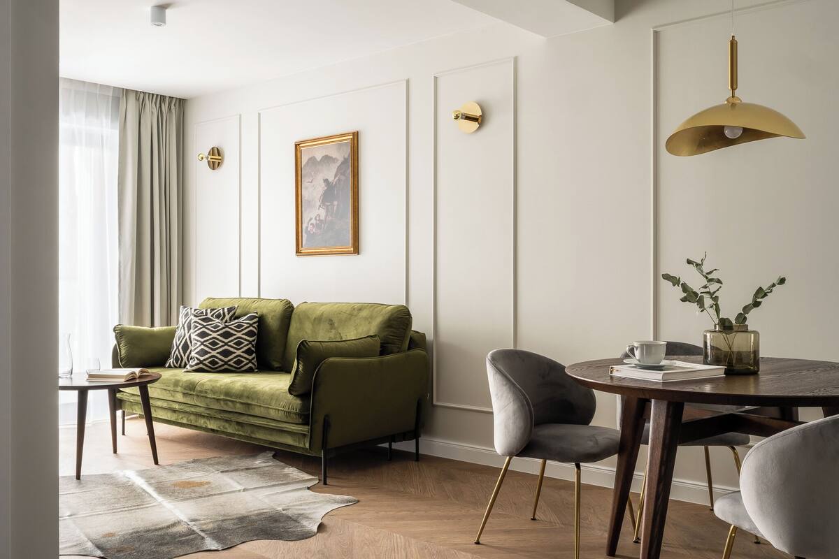 A modern living room with a green sofa, a round wooden table, and a grey chair.