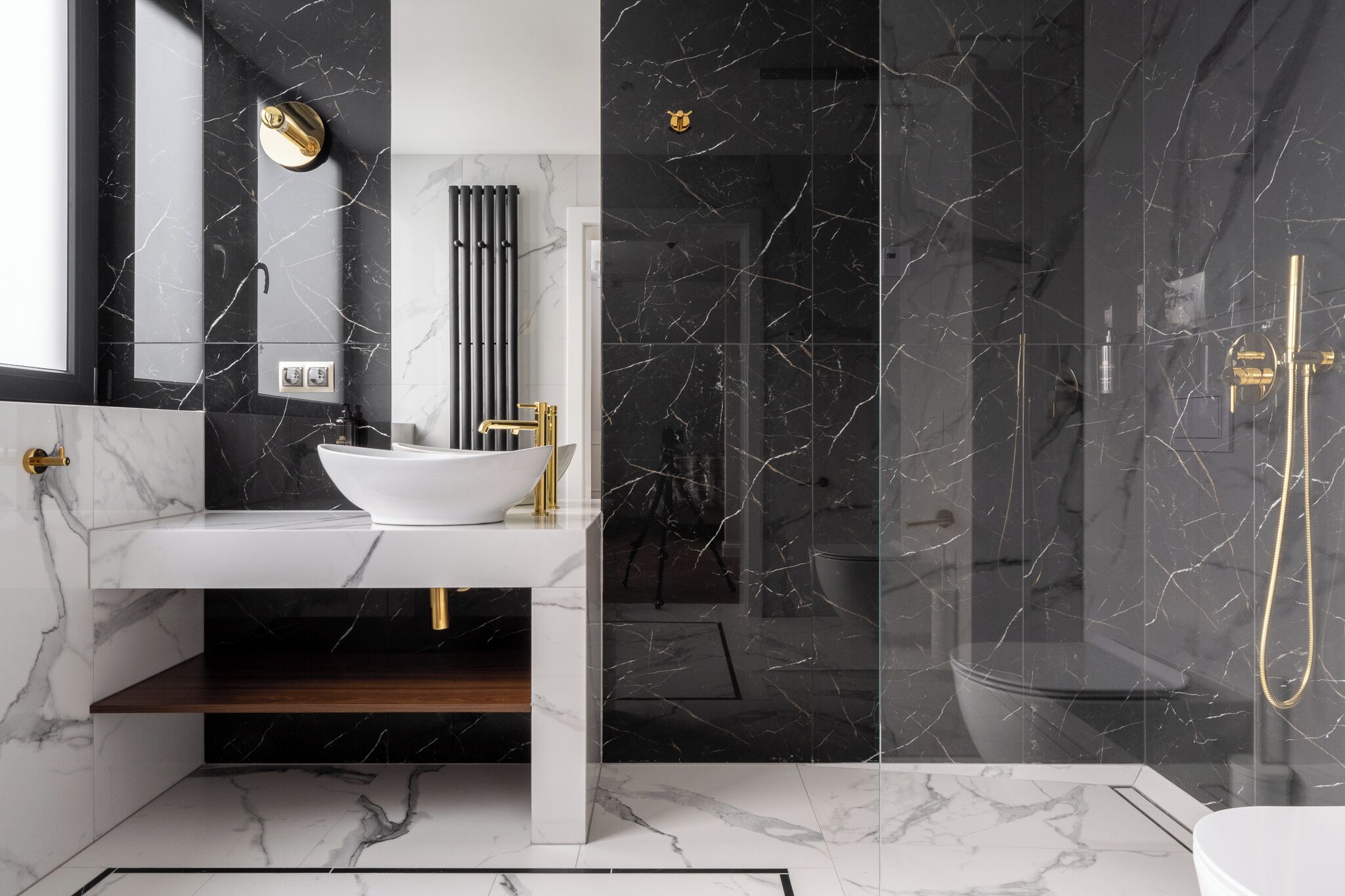 Een moderne badkamer met een wit wastafelmeubel, gouden details en een douche met glazen wanden.