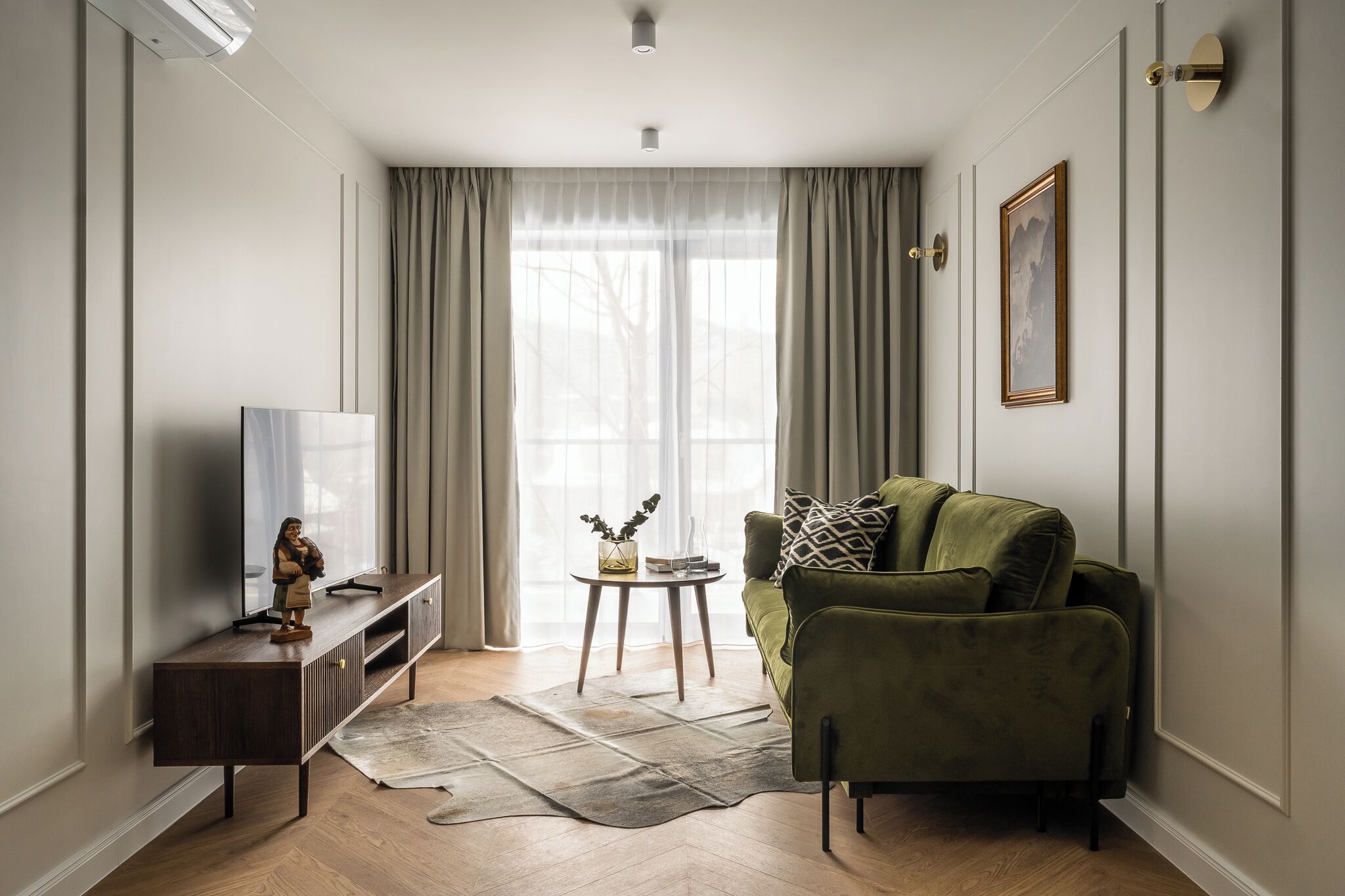 Ein modernes Wohnzimmer mit einem grünen Sofa, einem Holz-TV-Schrank und einem kleinen Beistelltisch mit einer Vase.