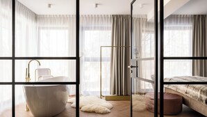 A modern bedroom with a large window, a bed, a vanity with a bathtub, and a glass partition. - Renesans Residence Zakopane (Zakopane)