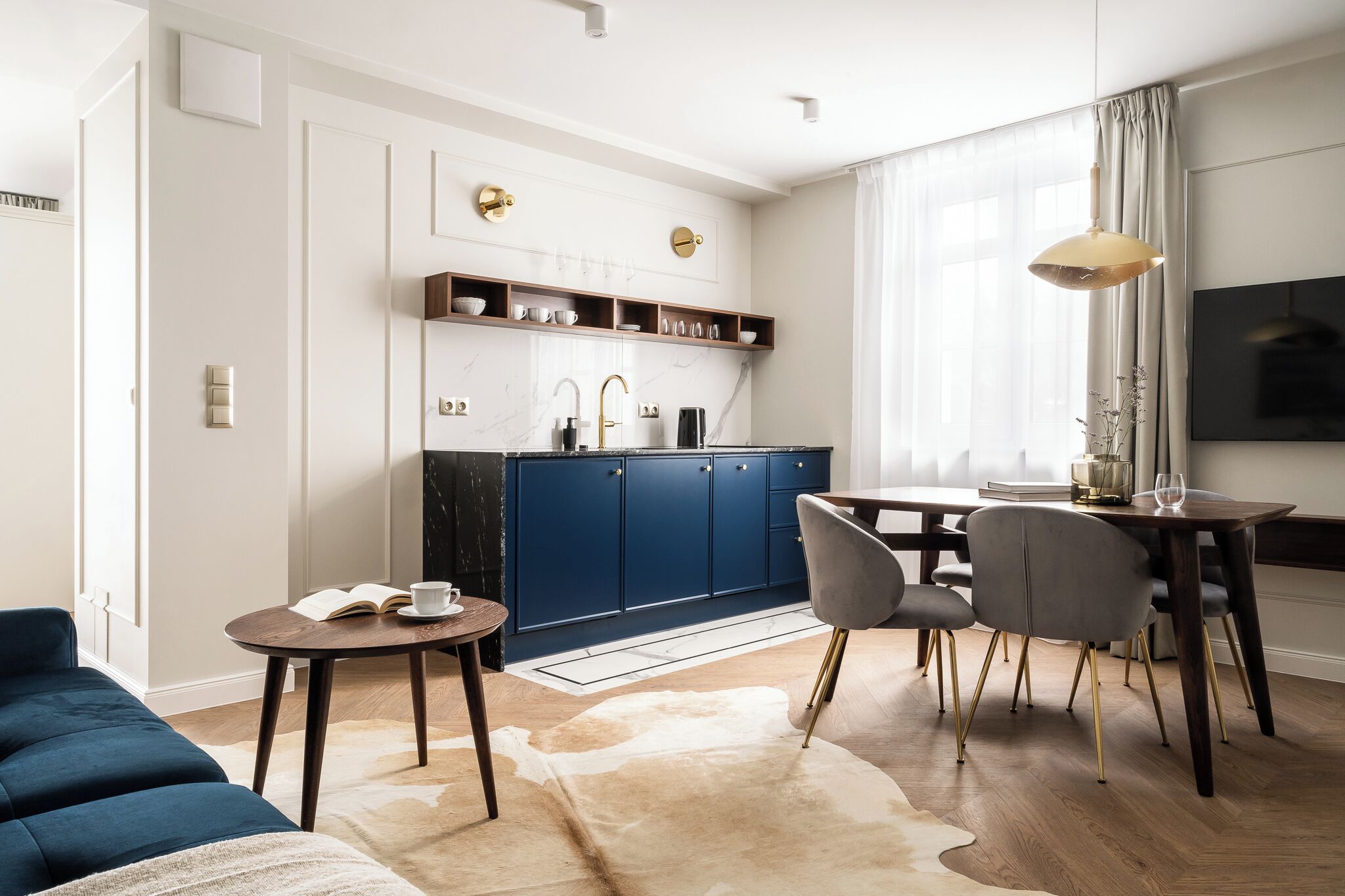 A modern kitchen with blue cabinets, a dining area with a table and chairs, and a living room with a blue sofa.