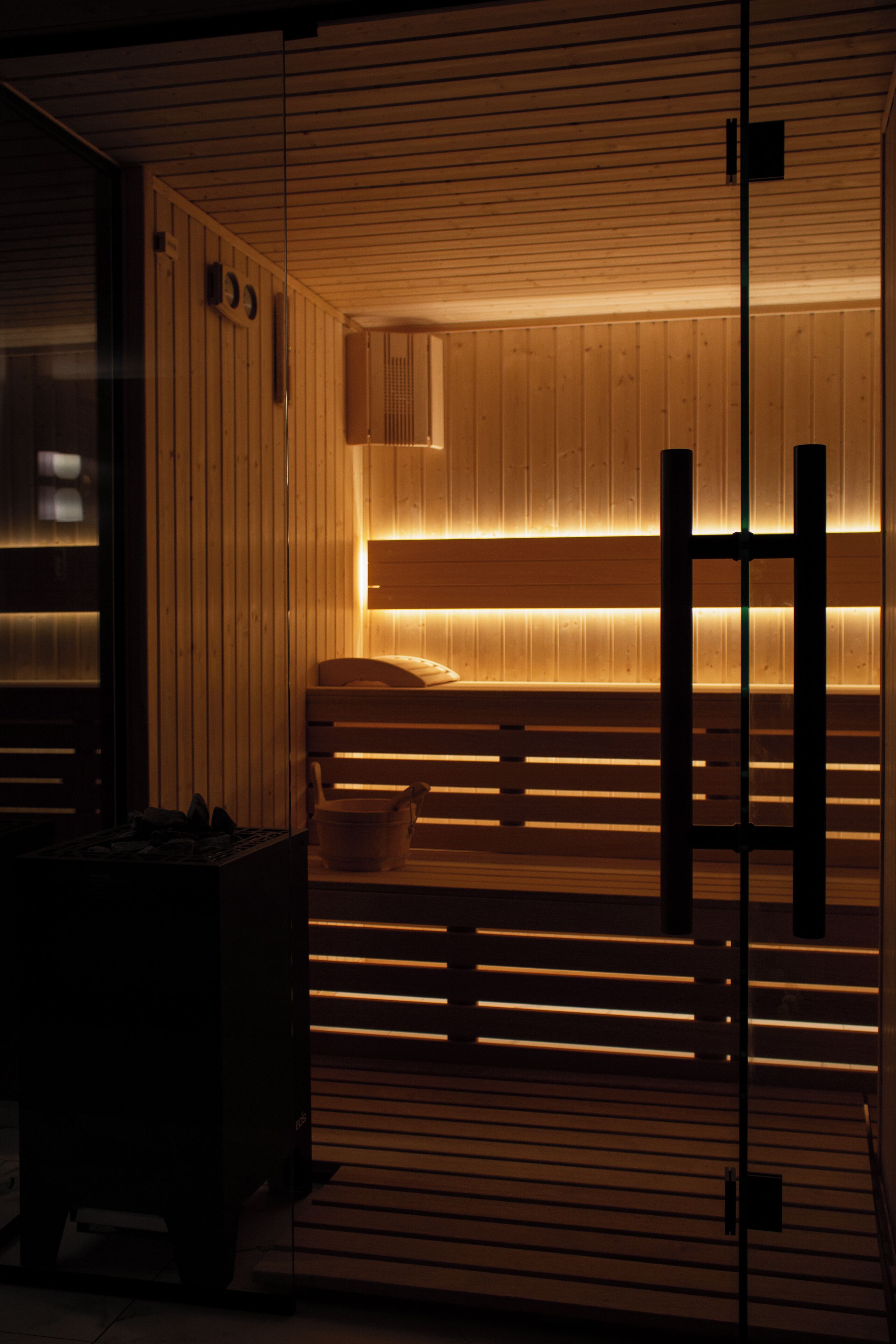 Un sauna avec des panneaux en bois et un banc, un radiateur fixé au mur, et une petite table avec un seau.