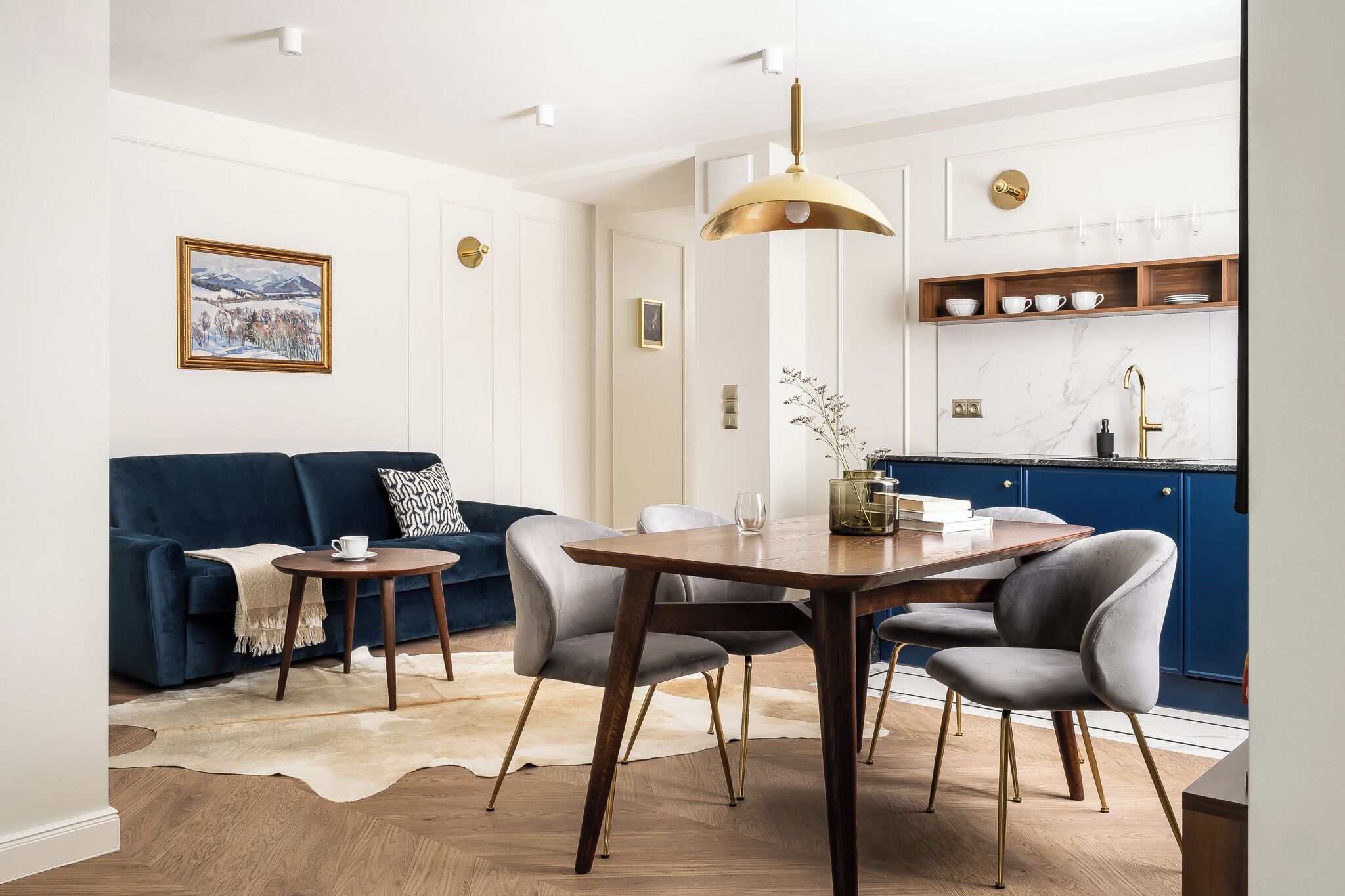 Un salon moderne avec un canapé bleu foncé, une table ronde en bois et un coin repas.