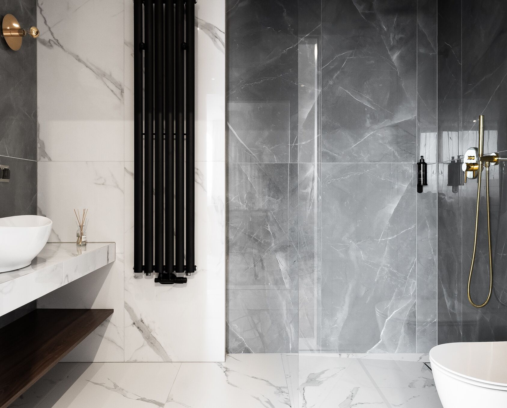 A modern bathroom with a white vessel sink, a black radiator, a glass shower enclosure, and a gold showerhead.