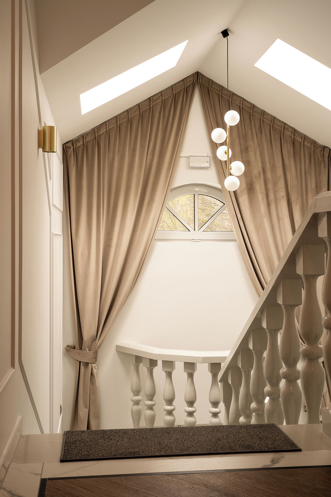 A staircase with a wooden handrail and a white balustrade, leading to a landing with a window and a light fixture.