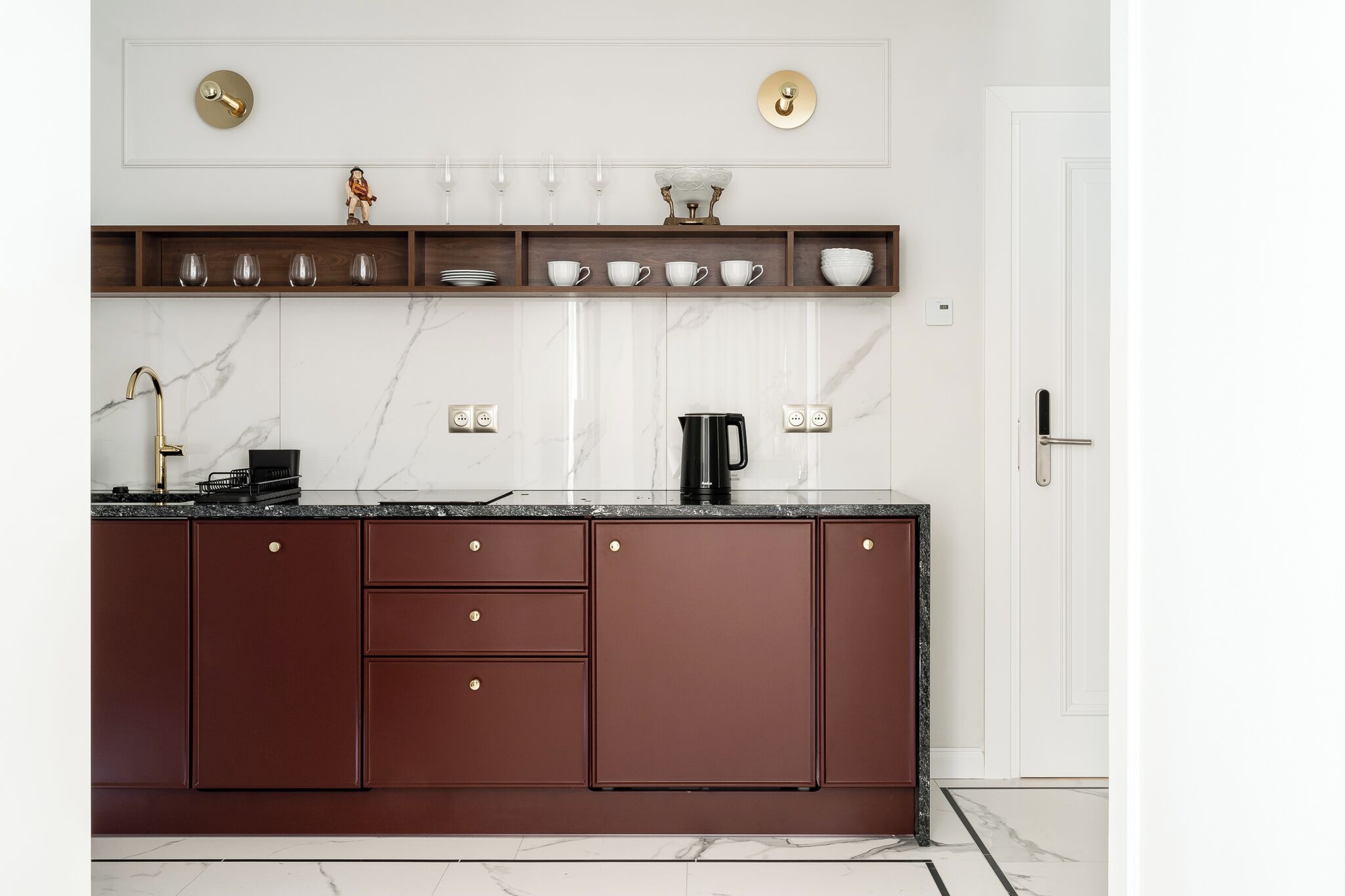 A modern kitchen with a marble countertop, dark cabinetry, and a coffee maker.