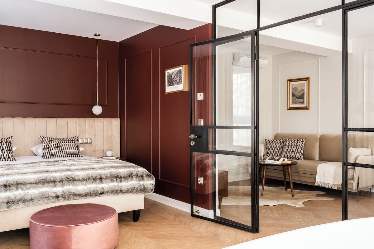 A modern bedroom with a large bed, a glass door leading to a living area, and a wooden floor.