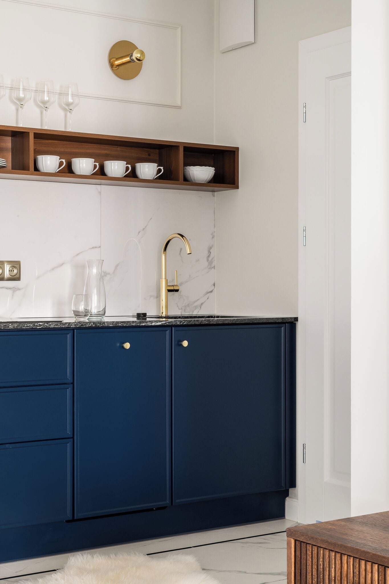 A modern kitchen with dark blue cabinets, a gold faucet, and a marble backsplash.