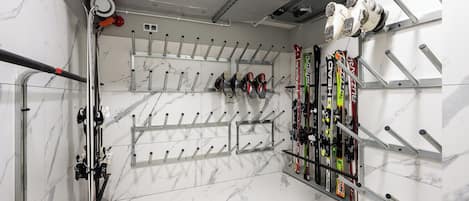 A ski storage area with multiple racks for skis and snowboards, a metal ceiling, and marble flooring.