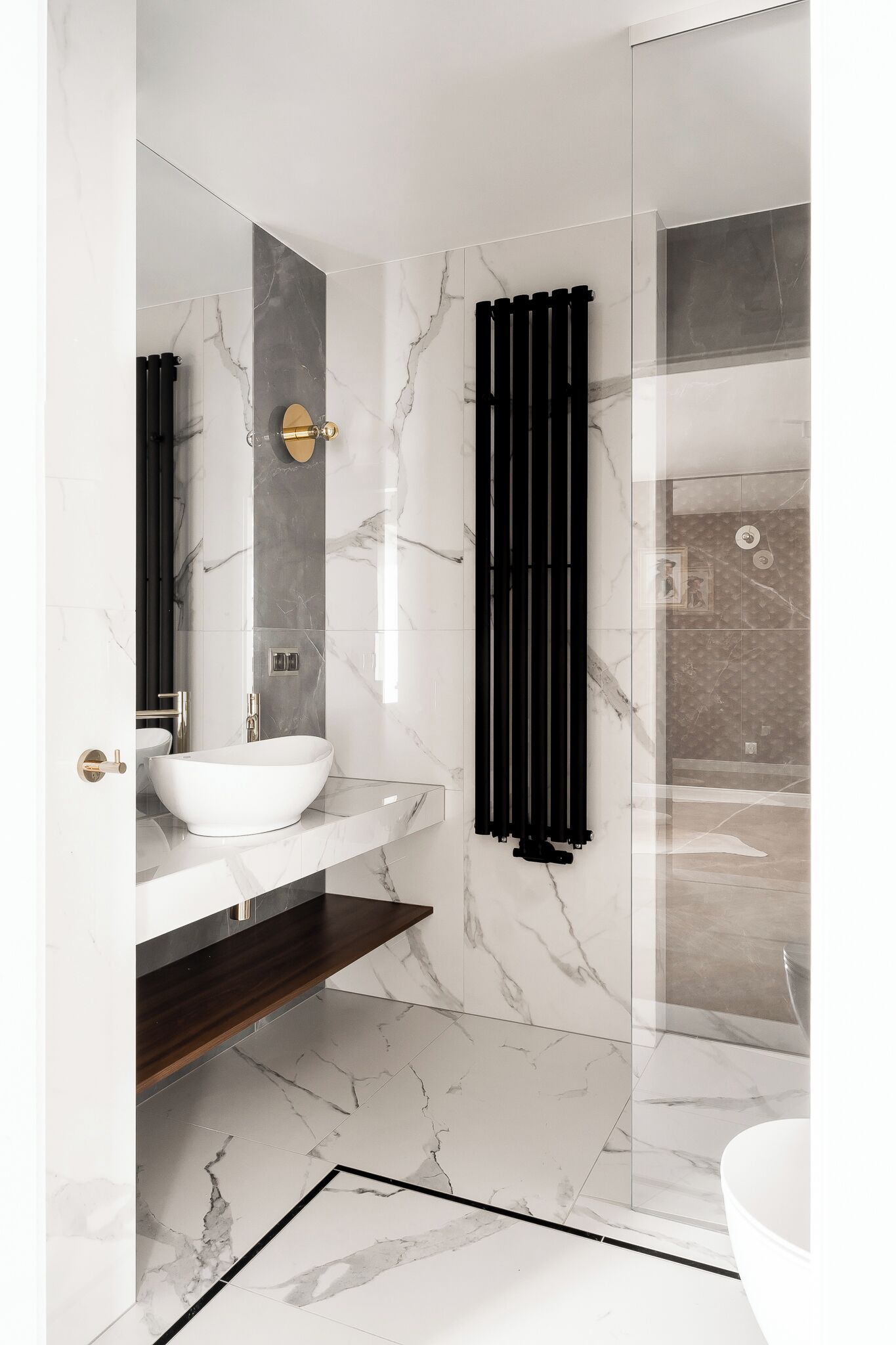 A modern bathroom with a white sink, marble walls, and a glass shower enclosure.