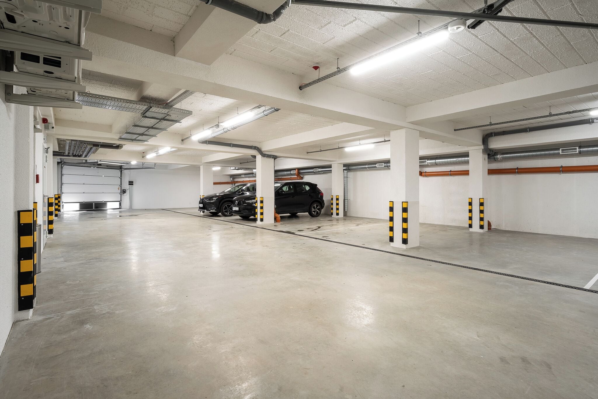 Un aparcamiento de varios niveles con suelos de hormigón y paredes blancas, que incluye varias plazas de aparcamiento y un SUV negro estacionado en una de ellas.