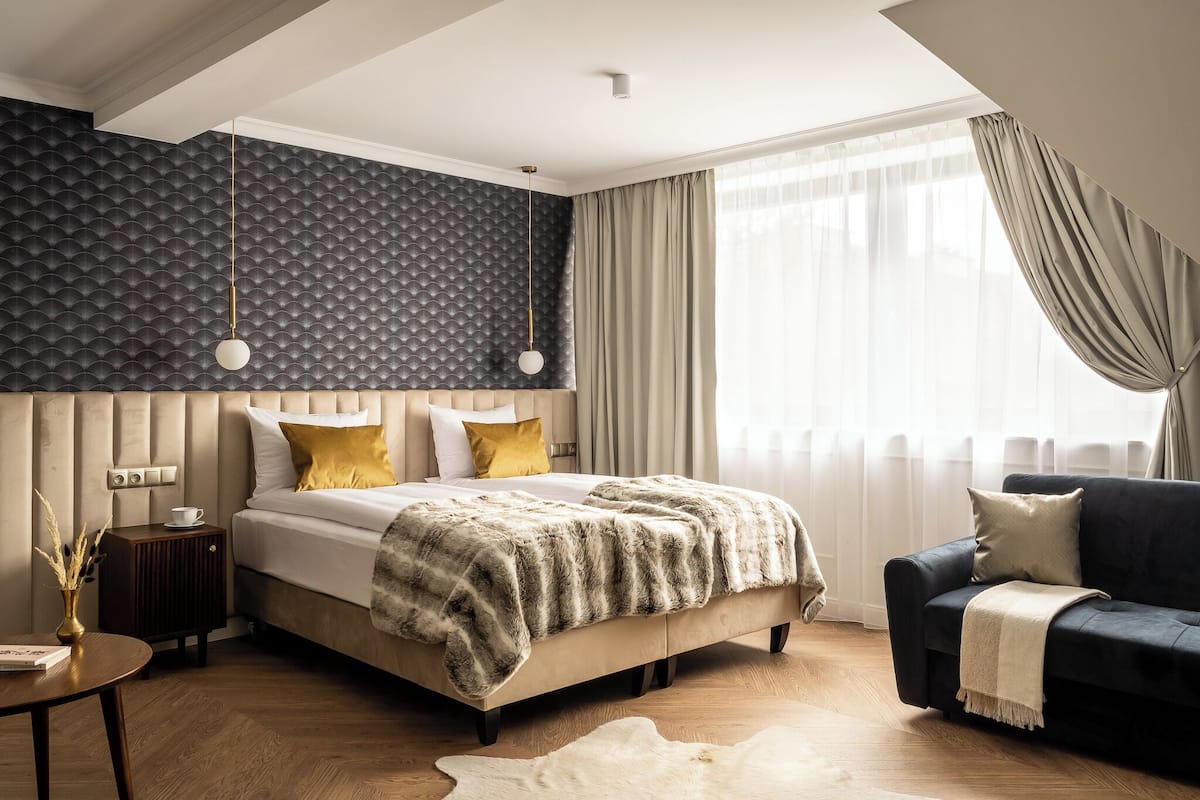 A modern bedroom with a large bed, a dark blue sofa, and a patterned wall.