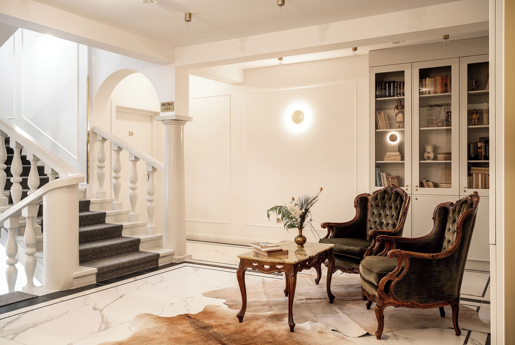 A grand staircase leading to a landing with a chandelier, a leather sofa, and a bookcase filled with books and decorative items.
