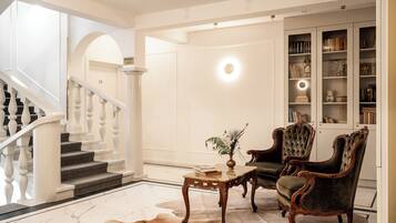 A grand staircase leading to a landing with a chandelier, a leather sofa, and a bookcase filled with books and decorative items.