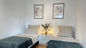 Een slaapkamer met twee eenpersoonsbedden, een nachtkastje met een lamp en een potplant.