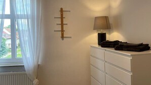 Een slaapkamer met een raam, een radiator, een witte dressoir en een lamp.
