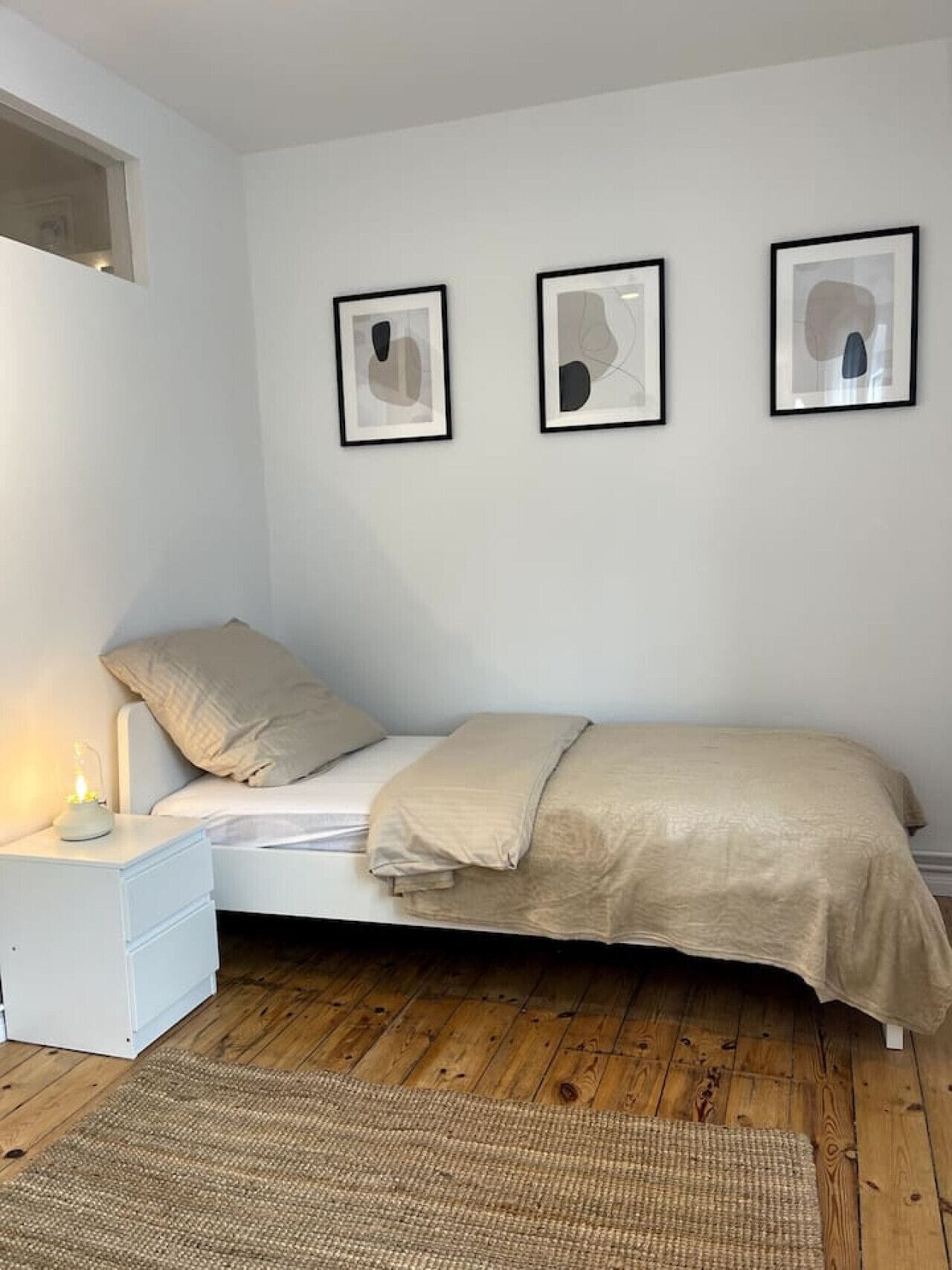 Une chambre à coucher avec un lit, une table de chevet et trois œuvres d’art abstraites encadrées accrochées au mur.