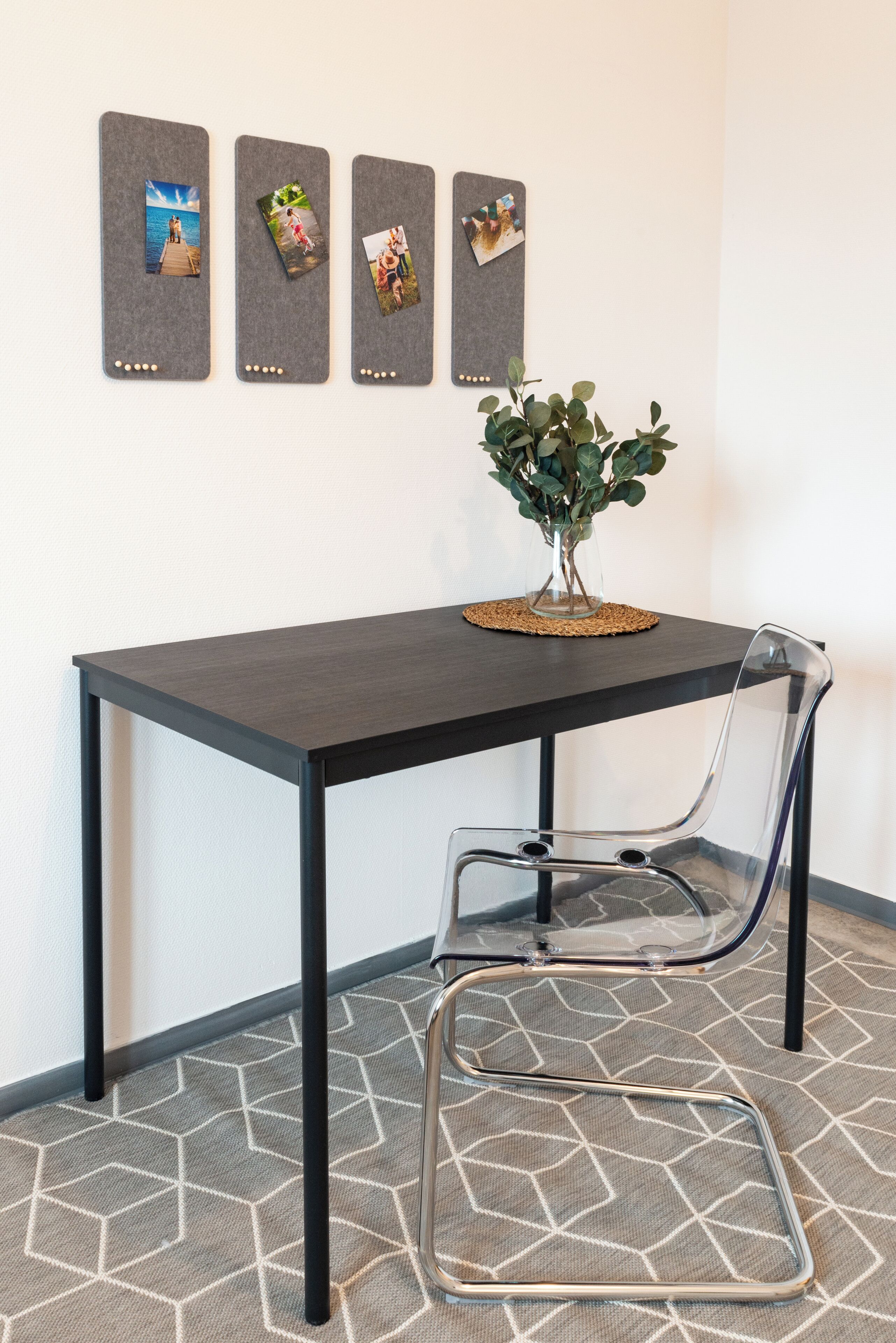 Une pièce moderne avec une table en bois foncé, une chaise transparente et un collage de photos accroché au mur.