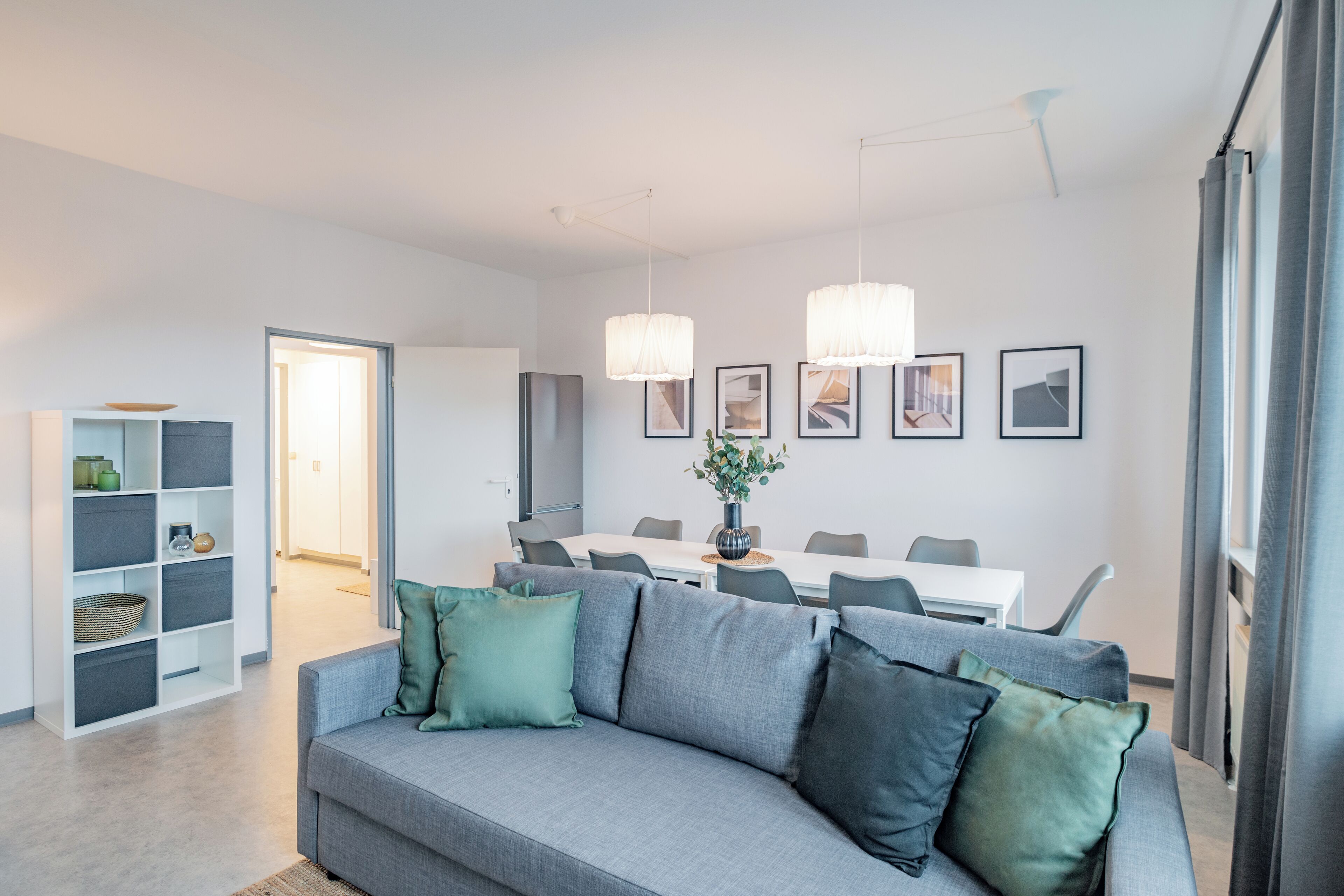 A modern living room with a grey sofa, a dining area with a white table, and a hallway leading to another room.