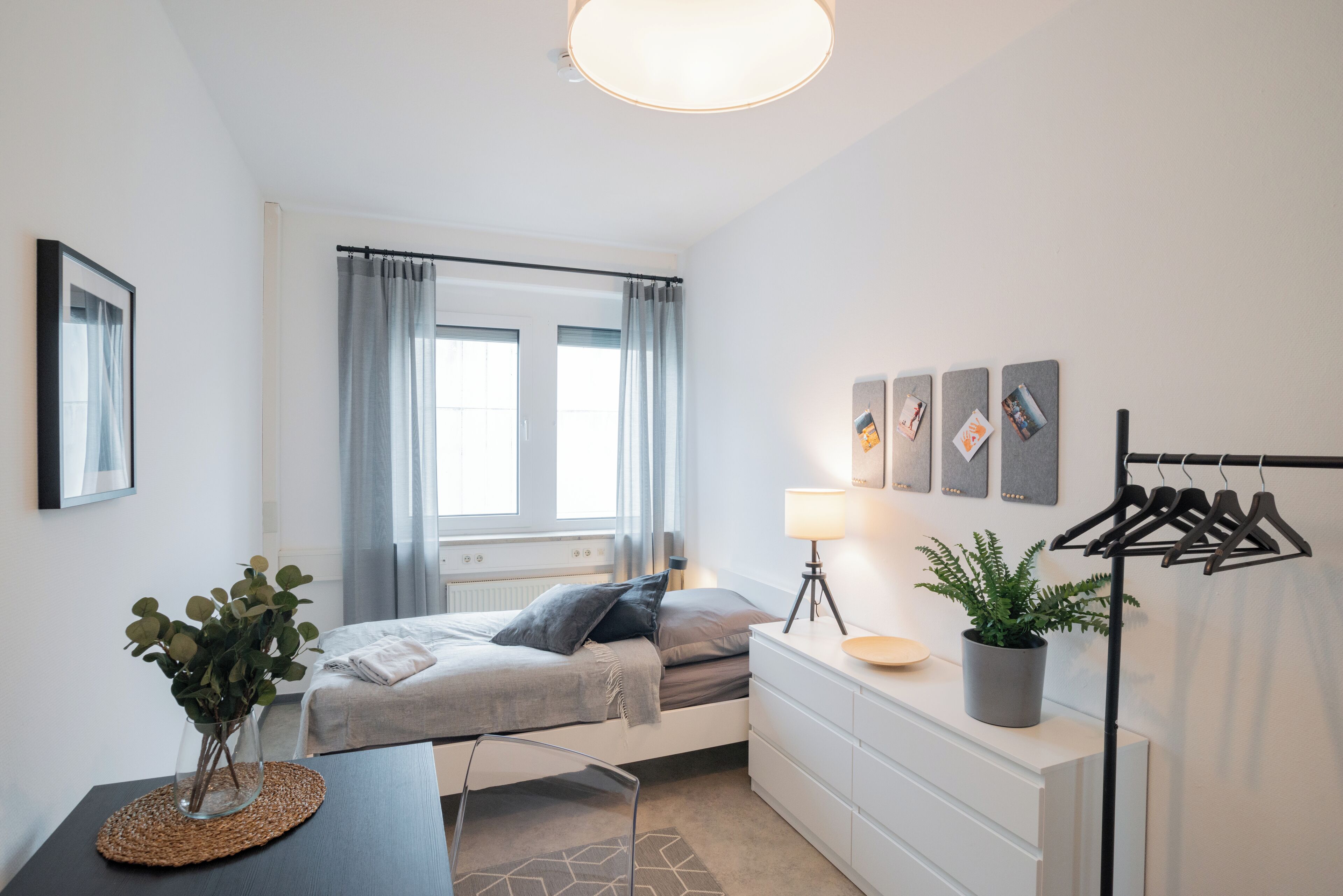 Et moderne soveværelse med seng, sengebord, lampe og et ophængt tøjstativ.