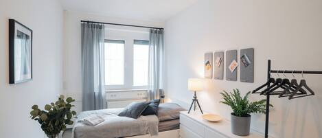 Et moderne soveværelse med seng, sengebord, lampe og et ophængt tøjstativ.