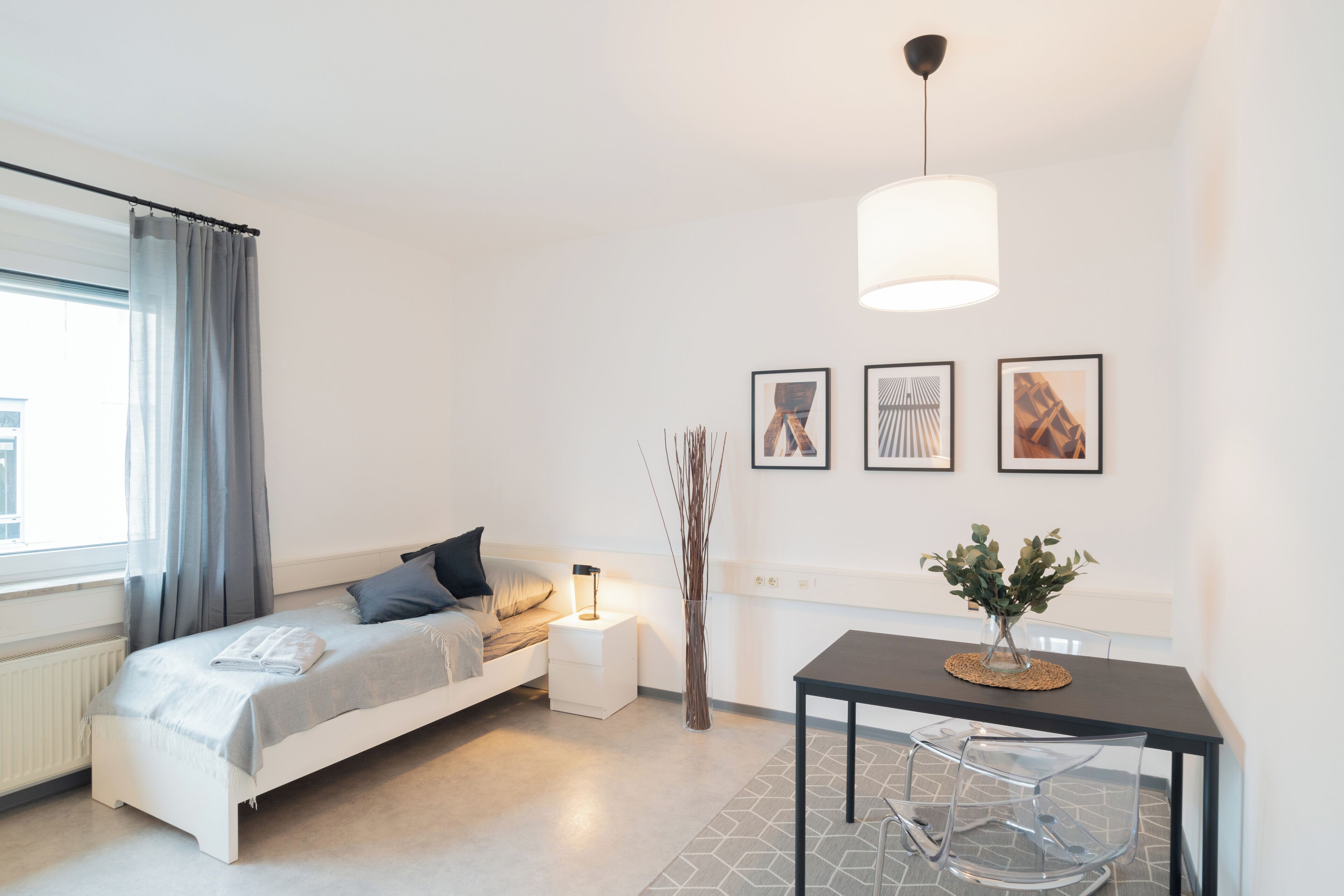 Un dormitorio moderno con cama, mesita de noche, lámpara y un rincón comedor con mesa y sillas.