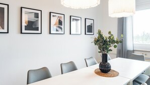 Ein moderner Essbereich mit einem weißen Tisch, grauen Stühlen, gerahmten Kunstwerken an der Wand und einem Blumentopf.