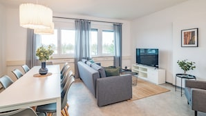 Ein modernes Wohnzimmer mit Sofa, Fernseher, Esstisch und Stühlen.