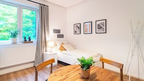 Ein modernes Hotelzimmer mit Bett, Nachttisch, Lampe und Blick auf Grünfläche.