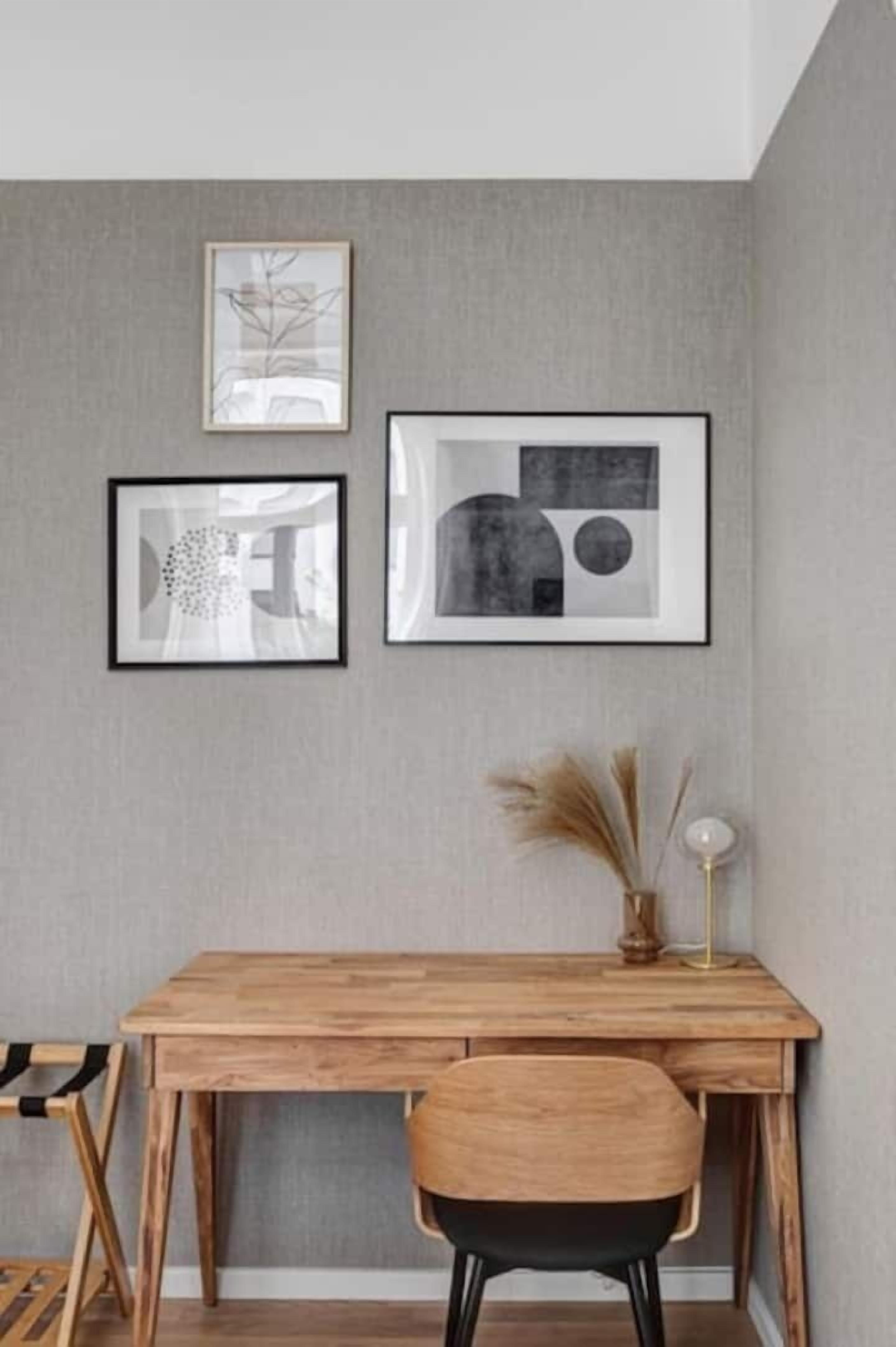 Ein Holztisch mit Stuhl, ein gerahmtes abstraktes Gemälde und eine Vase mit Trockenpflanzen.