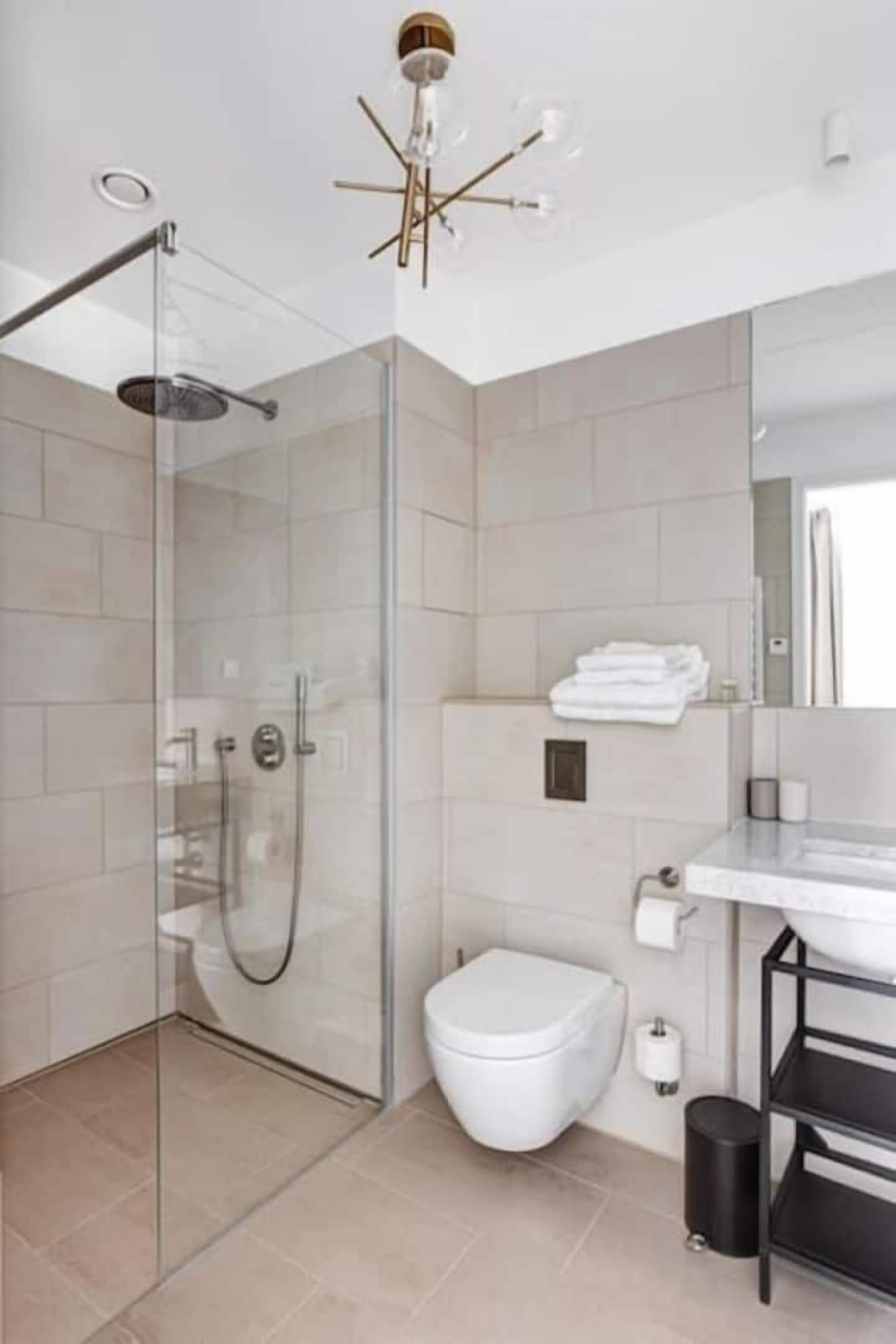 Un baño moderno con ducha envuelta en vidrio, inodoro blanco y estantería negra.