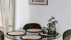 A modern dining area with a round glass table, green upholstered chairs, and a chandelier with clear glass globes. - Arbio I Luxury Apartments (Berlin)