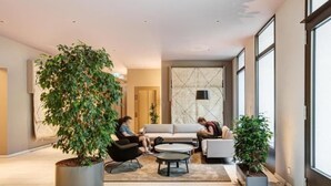 A modern hotel lobby with a large indoor plant, seating area, and large windows. - Arbio I Luxury Apartments (Berlin)
