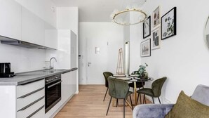 A modern kitchen with white cabinets, a built-in oven, and a dining area with a round table and chairs. - Arbio I Luxury Apartments (Berlin)