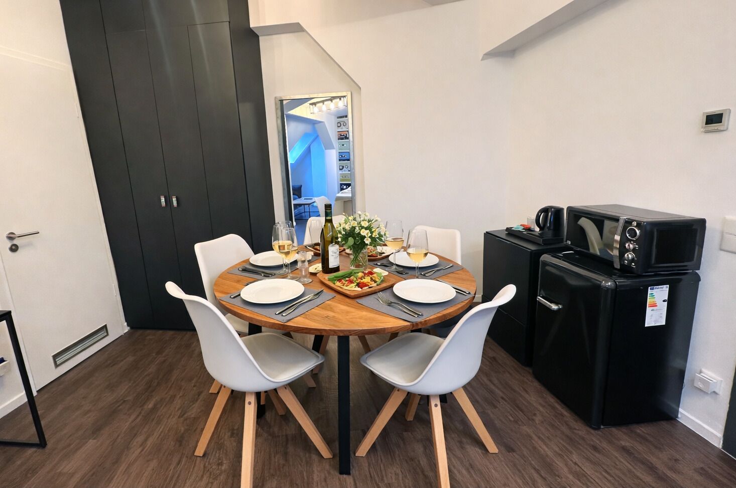 Un comedor pequeño con una mesa redonda, cuatro sillas, un refrigerador negro y una kitchenette.