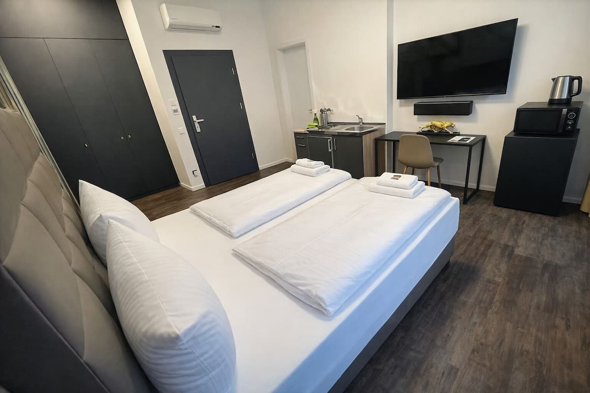 A hotel room with a bed, a desk, a chair, a TV, and a coffee machine.