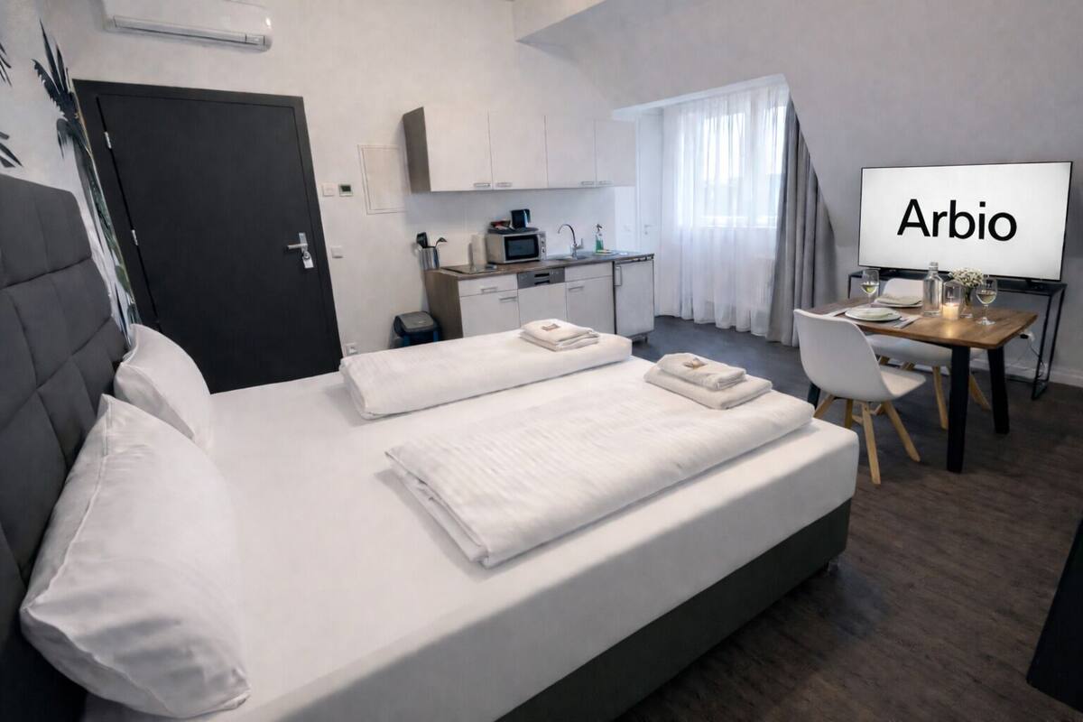 A hotel room with a bed, a desk, a chair, a TV, and a kitchenette.