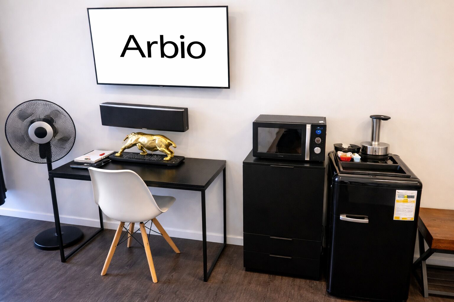 A compact room with a desk, chair, fan, microwave, and refrigerator.