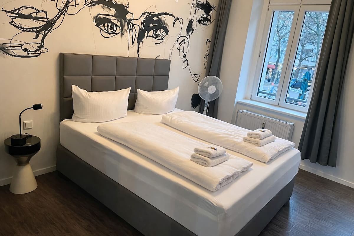 A double bed with white linens, a grey headboard, and a wall mural.